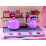 Lalka w pastelowej sukience i fartuszku stojąca przy meblach